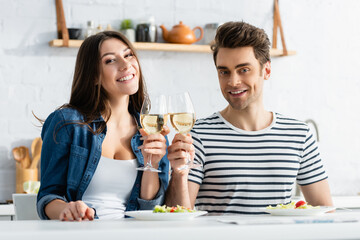 happy couple clinking glasses of wine near plates with salad in kitchen