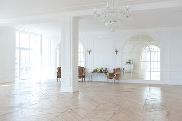 chic white huge spacious hall with a minimum of expensive antique furniture. Baroque interior design with ornament on the walls and parquet on the floor.