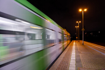 Night outdoor scenery of platform railway station and regional train with blur motion.