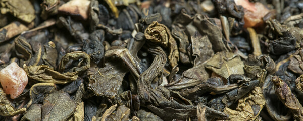 Dried green and black tea mix leaves with pieces of fruits background.