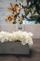 Detail of dining room table with white flowers in gray container, gray fabric chairs and yellow sunflower wall covering.