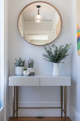 Detail of home entry hall with white and gold side table, plant decor and round mirror.