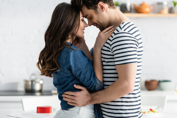 side view of happy couple with closed eyes hugging in kitchen