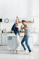 full length of excited couple dancing in modern kitchen