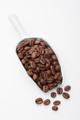 Dark roasted coffee beans in metal scoop on a light background