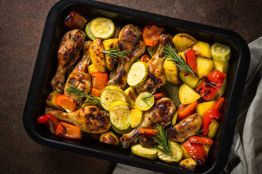 Baked chicken with vegetables preparing in the oven at baking sheet. Top view.