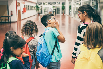 Group of schoolkids with colorful backpacks walking in school corridor and chatting. Back view. Education or back to school concept