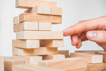 Planning, risk and strategy in business, businessman gambling placing wooden block on a tower. The tower from wooden blocks and man's hand take one block