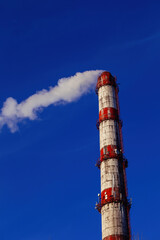 Red and white smoking industrial pipe against the blue sky