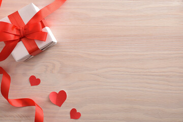 White gift with bow and heart-shaped cutouts on wooden table