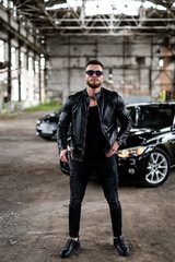 Handsome young man in leather jacket holding a gun. Cool sunglasses on brutal man.