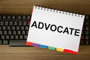 the word advocate is written on a white notepad that lies on the computer keyboard