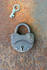 Closed old rusty lock with key lying near on the rusty iron surface. Copy space.looking for problem...