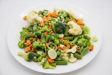 Frozen vegetables: cauliflower, green peas, leeks, broccoli, carrots, green beans on a white plate.