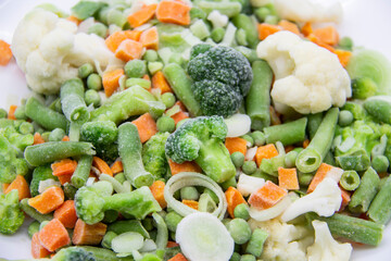 Frozen vegetables: cauliflower, green peas, leeks, broccoli, carrots, green beans on a white plate.