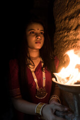 beautiful Indian girl in old stepwell wearing traditional Indian red saree, gold jewellery and...