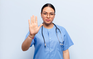 hispanic woman looking serious, stern, displeased and angry showing open palm making stop gesture
