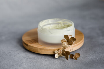 A jar of face cream on a wooden stand on a gray background.