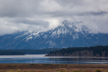 A Teton Mountain with snow and clouds and a lake in the foreground