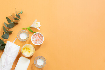 Creative composition with natural cosmetic products for spa and bath, aromatic candles and beautiful flowers on light beige background with copy space for your design. 