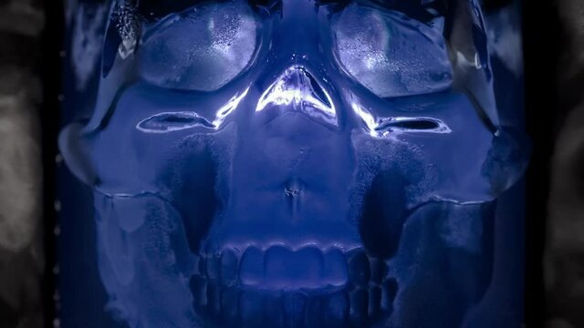 Glowing Blue Glass Skull. Ice skull glowing with a cold blue light in the vapor of evaporating gas. Slow Motion 240 fps