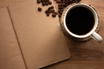 selective focus, cup of coffee, coffee beans  and notebook for take note on wooden table. For to do list or goals list concept photo. top view with copy space for your text.