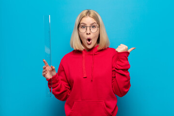 blonde woman looking astonished in disbelief, pointing at object on the side and saying wow,...