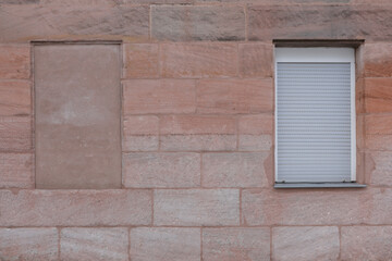 Red brick wall with one window, rolled up aluminum shutter, and a frame with stones, symbol for lockdown, space for text, 
no person