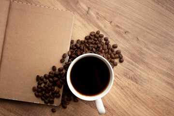 Selective focus coffee mug on wooden work table in office. Top view; Coffee, coffee beans, notebook  for to do list or goals list background working lifestyle. copy space.