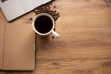 Selective focus coffee mug on wooden work table in office. Top view; Coffee, coffee beans, notebook  for to do list or goals list background working lifestyle. copy space.