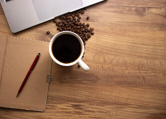 Obraz na płótnie Canvas Selective focus coffee in mug on wooden work table. coffee lovers lifestyle. Coffee, coffee beans, notebook, red pen for to do list or goals list background working lifestyle. copy space. 