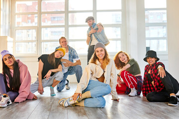 woman in casual wear with colleagues dancers posing at camera in studio, sit on the floor looking at camera. party, dance, youth concept