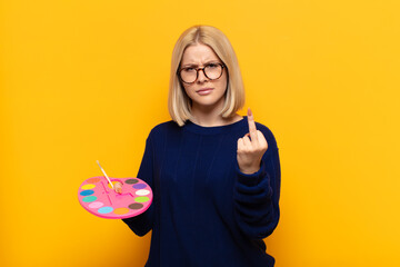 blonde woman feeling angry, annoyed, rebellious and aggressive, flipping the middle finger,...