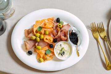 Seafood platter with salmon slice, black caviar, decorated with olive on white plate.