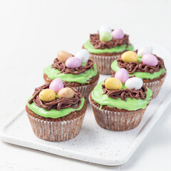 Homemade carrot cupcakes with cream cheese frosting and Easter chocolate eggs, on a white plate, square format