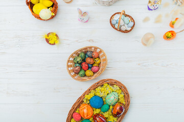 Multi-colored Easter eggs in a basket on a white wooden background