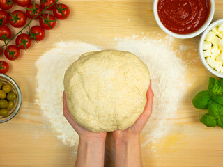 Hands hold the raw dough for pizza. Cooking pizza. Table with ingredients: tomato sauce, cherry...