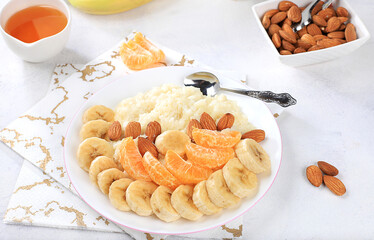Useful breakfast with ingredients, flat lay, rice pudding with bananas, honey, tangerines and almonds on a sunny table. Healthy and natural food concept, lifestyle, food for children,