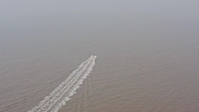 Aerial drone shot towards a speed boat on muddy water hazy day