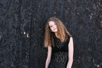 Naklejka premium Red-haired girl in a black dress near a dark textured wall