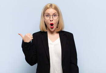 blonde woman looking astonished in disbelief, pointing at object on the side and saying wow,...