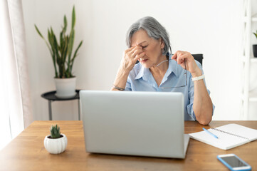 Tired and overworked stressed mature woman working on laptop at home indoor, female teacher feeling...