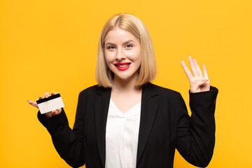 blonde woman smiling and looking friendly, showing number four or fourth with hand forward,...