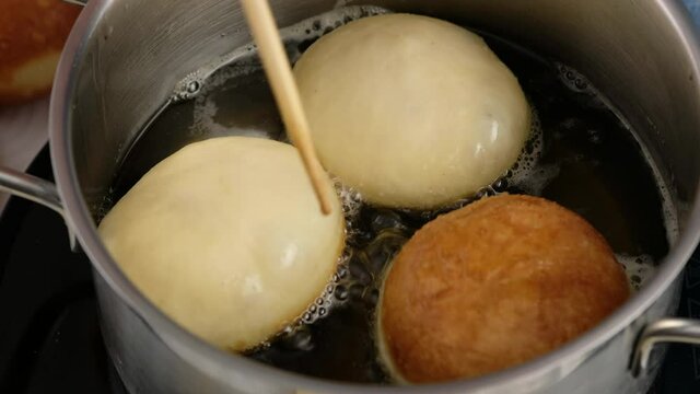 Berliners. Rolling donuts in oil. Donuts are fried in vegetable oil. Delicious sweet donuts. Making donuts with jam.