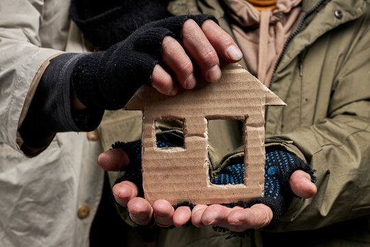 close-up photo of homeless people holding home made from cardboard in hands, need help and shelter, family concept