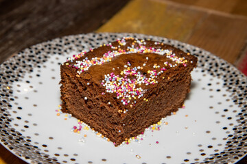 A delicious chocolate brownie cake slice topped with sprinkles on a wooden kitchen work top