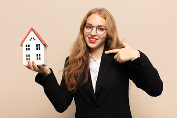 blonde woman smiling confidently pointing to own broad smile, positive, relaxed, satisfied attitude