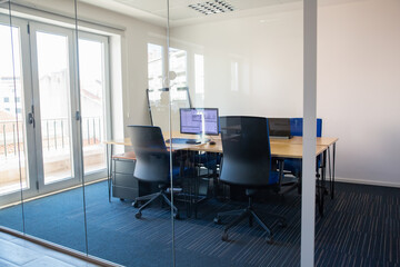 Empty boardroom behind glass wall. Meeting room with conference table, shared desk for team and...