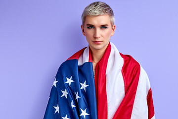 gay man is wrapped in american flag, posing isolated on purple backrgound. LGBT, transgender