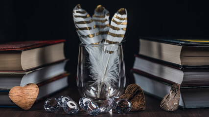 decorative concept with feathers in coffee glass, books and wooden hearts dark background
